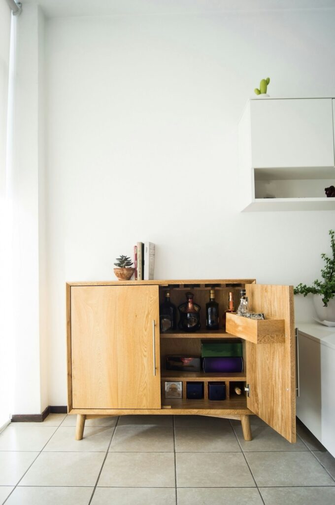 Vertical shot of a wooden alcohol cabinet in the room with the white wall on the background