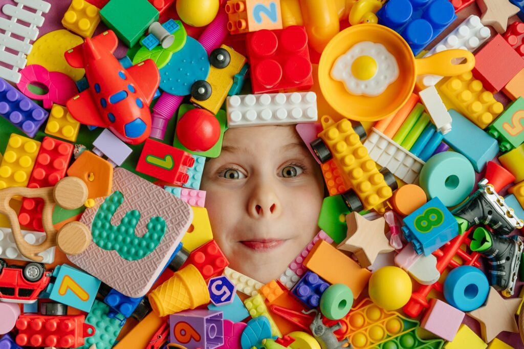 Little girl lying in the mess of toys. Top view, flat lay.