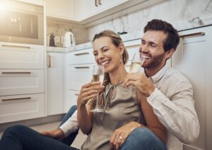 Laughing, love and couple with champagne in the kitchen for celebration, anniversary and valentines